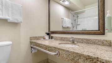 A bathroom with a granite countertop, a sink, a toilet, a shower, and a mirror with a wooden frame.