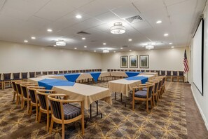 A conference room with multiple tables and chairs, arranged in a U-shape, with ceiling lights and an American flag on the wall. - Best Western Crossroads Inn (De Funiak Springs)