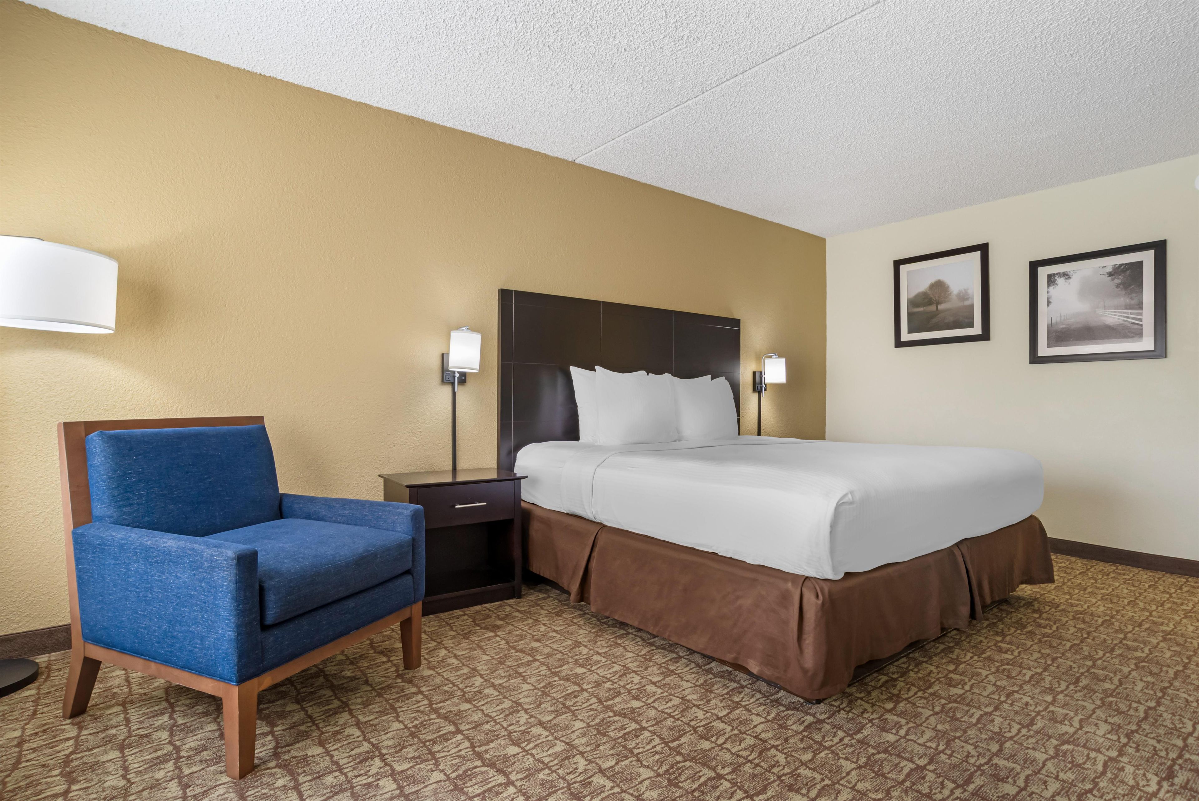 Une chambre d’hôtel comprenant un lit, une chaise, une table de chevet et deux lampes fixées au mur.