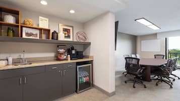 Una cocina moderna con encimera de granito, armarios empotrados y un refrigerador. Hay una cafetera y un lavabo. Se observa un área de comedor con una mesa y sillas al fondo.