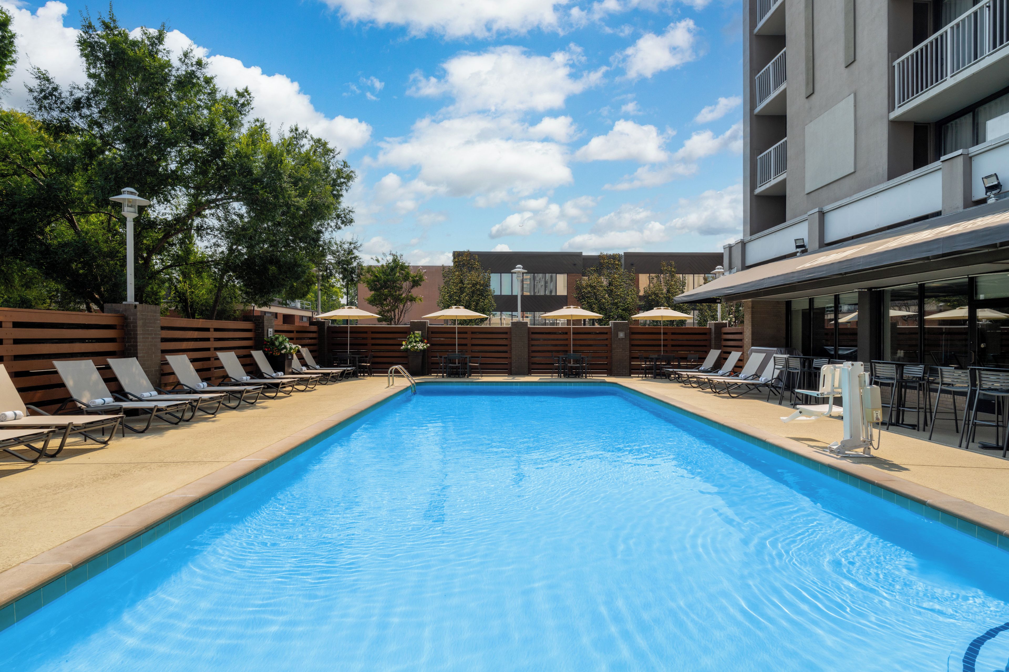 A swimming pool with lounge chairs and umbrellas, surrounded by a fence and trees.