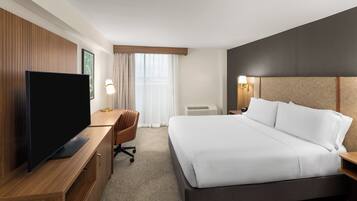Habitación de hotel con una cama grande, un televisor sobre un escritorio de madera, una silla y una ventana con cortinas.