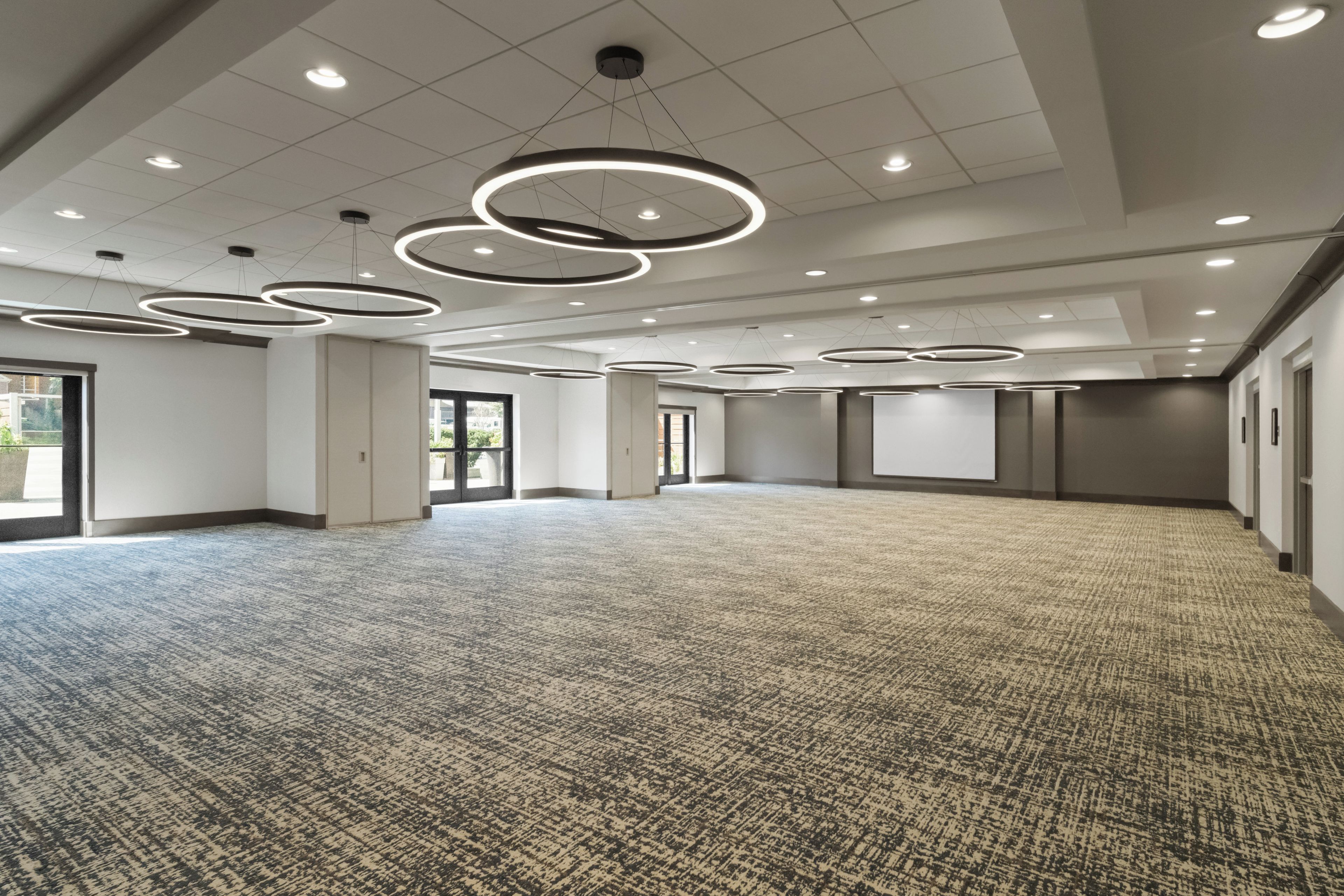 Une salle de conférence spacieuse, dotée d’un tapis à motifs, de luminaires circulaires au plafond et de grandes fenêtres laissant entrer la lumière naturelle.