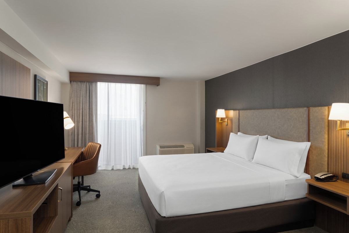 Een hotelkamer met een bed, een bureau met een flatscreen televisie, een stoel, een nachtkastje met een lamp en een telefoon.