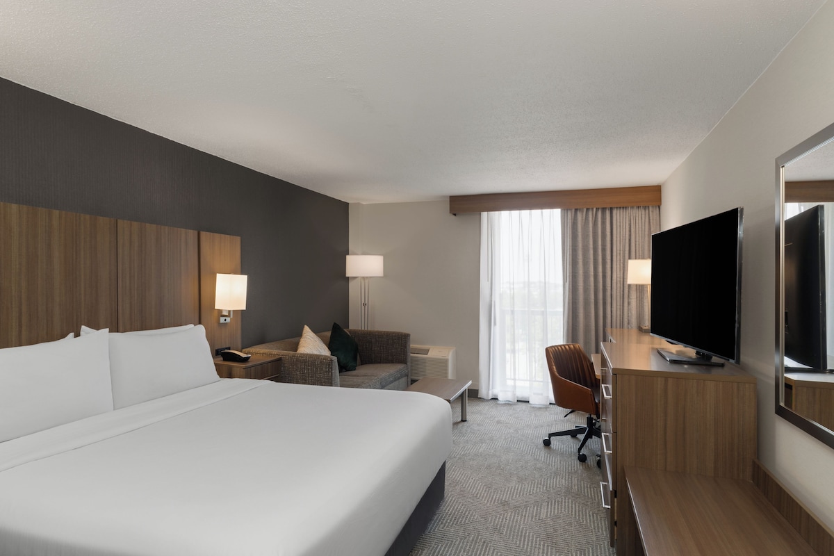 Een hotelkamer met een groot bed, een bureau met een flatscreen televisie, een stoel, een bank en een raam met gordijnen.