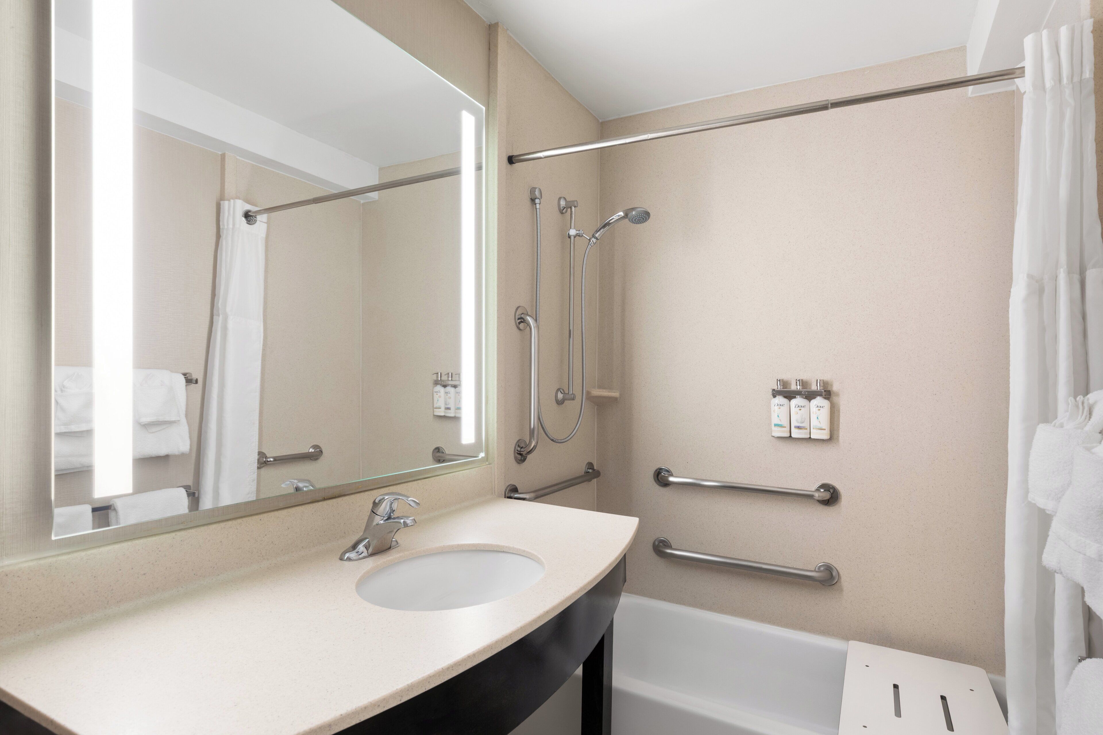 A bathroom with a sink, mirror, shower, and grab bars.