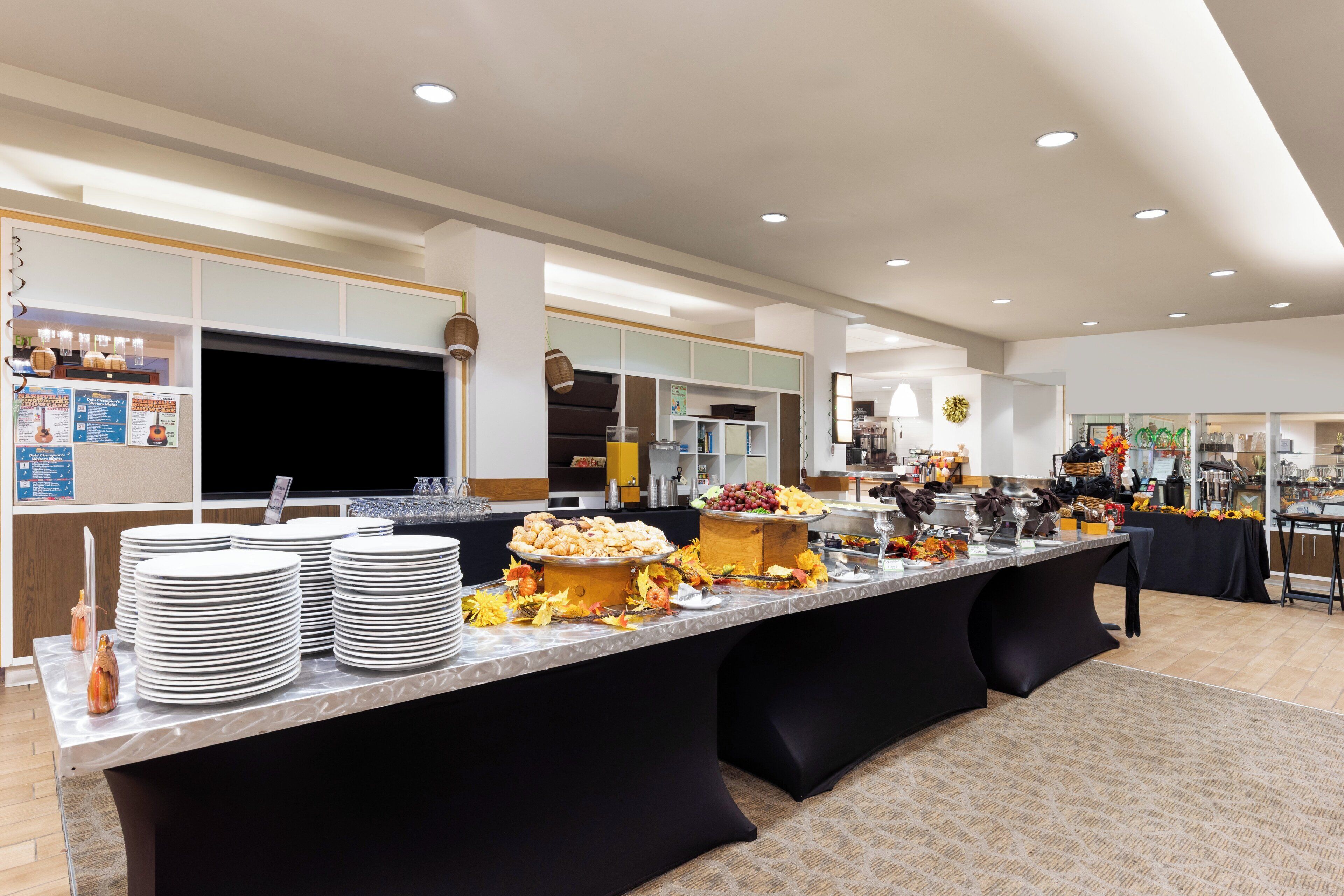 Uma mesa de buffet com várias estações de serviço, uma grande variedade de alimentos e pratos empilhados de forma organizada.