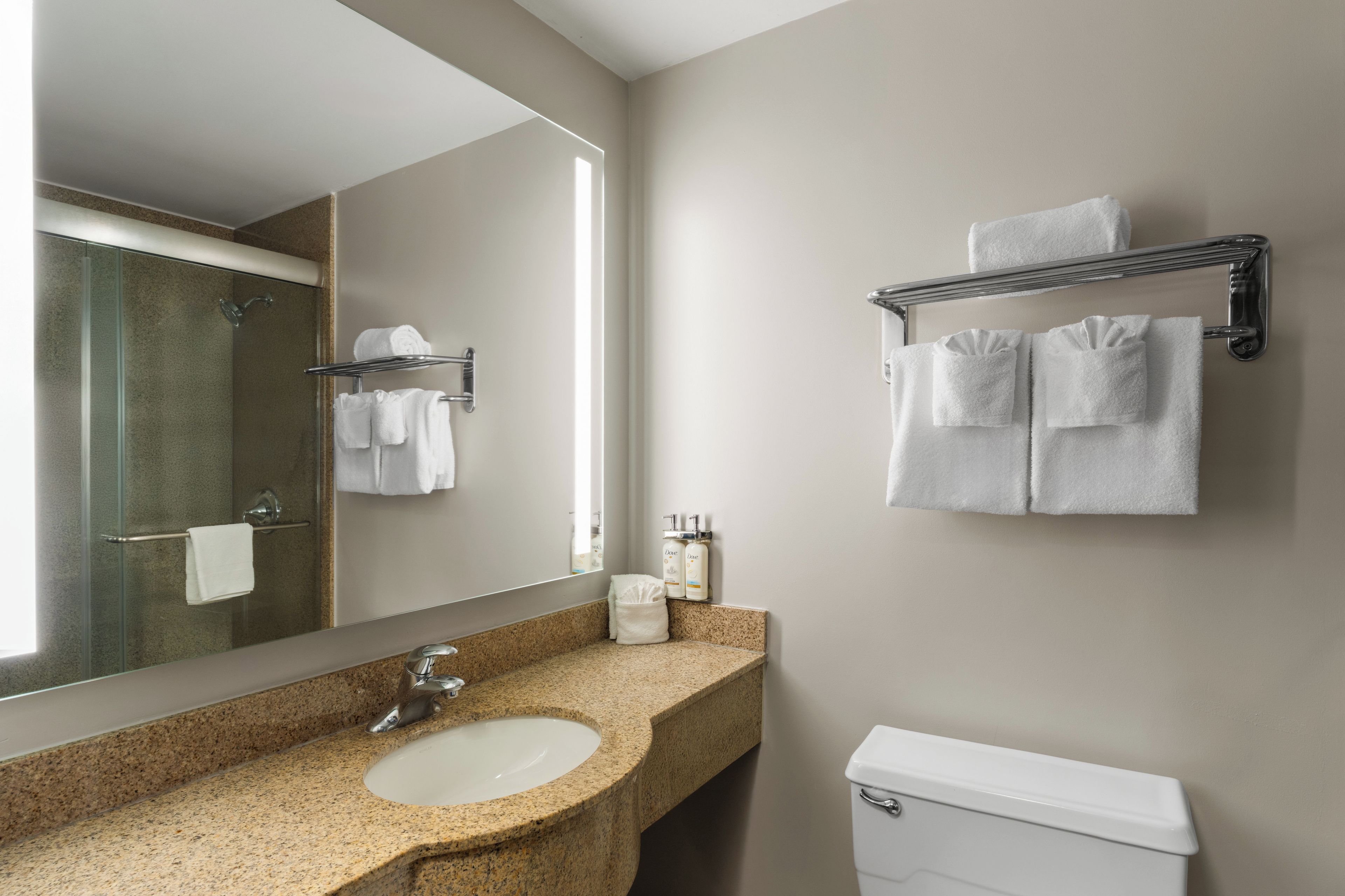 A bathroom with a granite countertop sink, a mirror, a towel rack with towels, and a toilet.