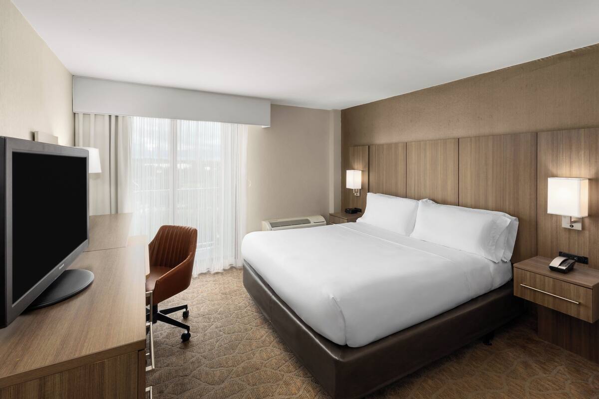 Een hotelkamer met een groot bed, een bureau met een flatscreen-tv, een stoel en twee nachtkastjes met lampen.