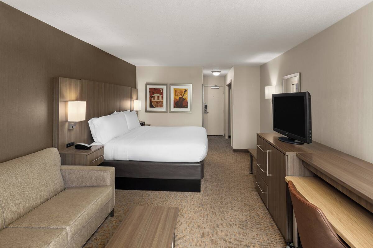 Een hotelkamer met een bed, een bank, een bureau, een televisie en twee foto's in lijsten aan de muur.