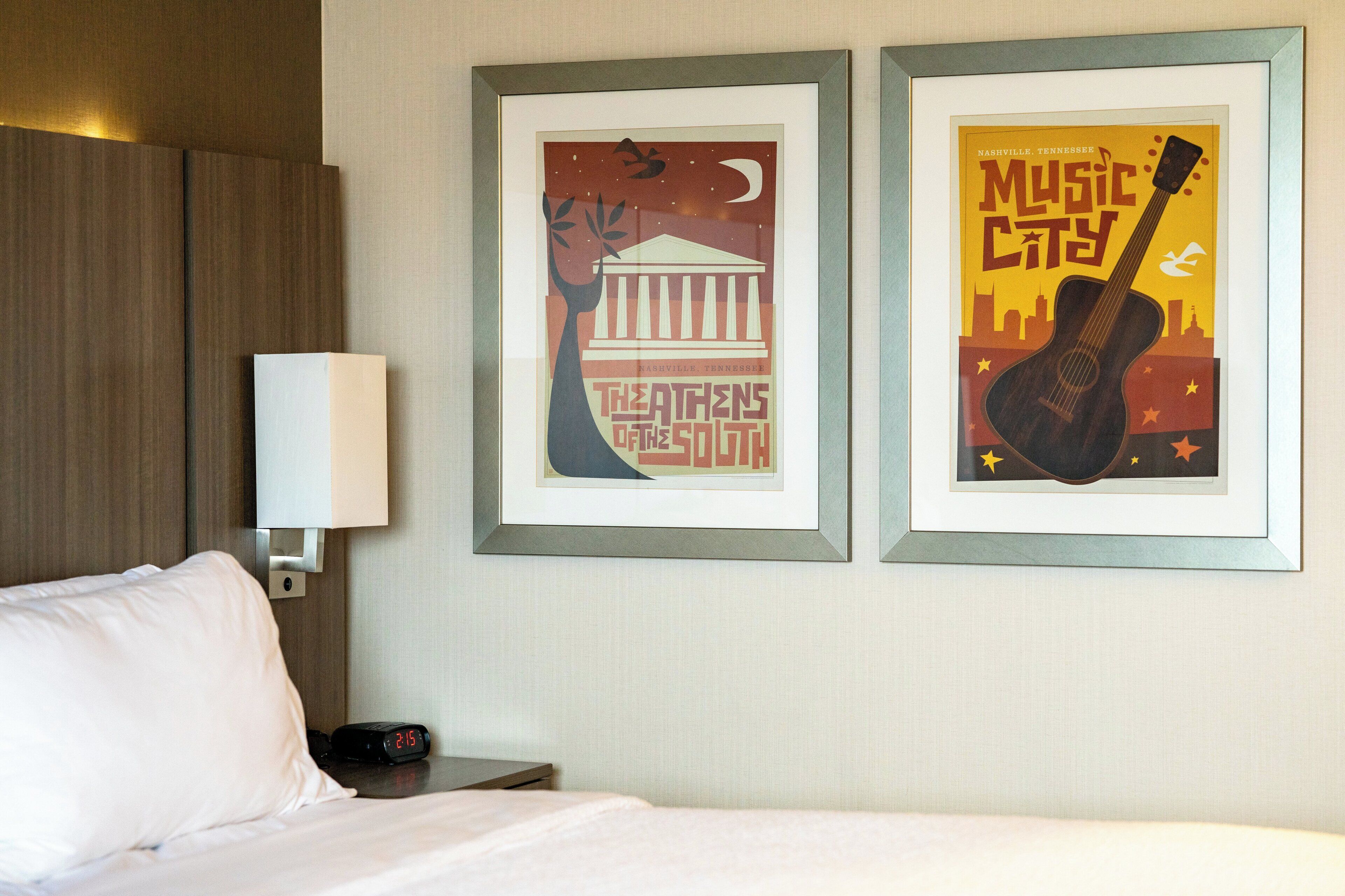 A hotel room with a bed, a nightstand, a lamp, and two framed posters on the wall.