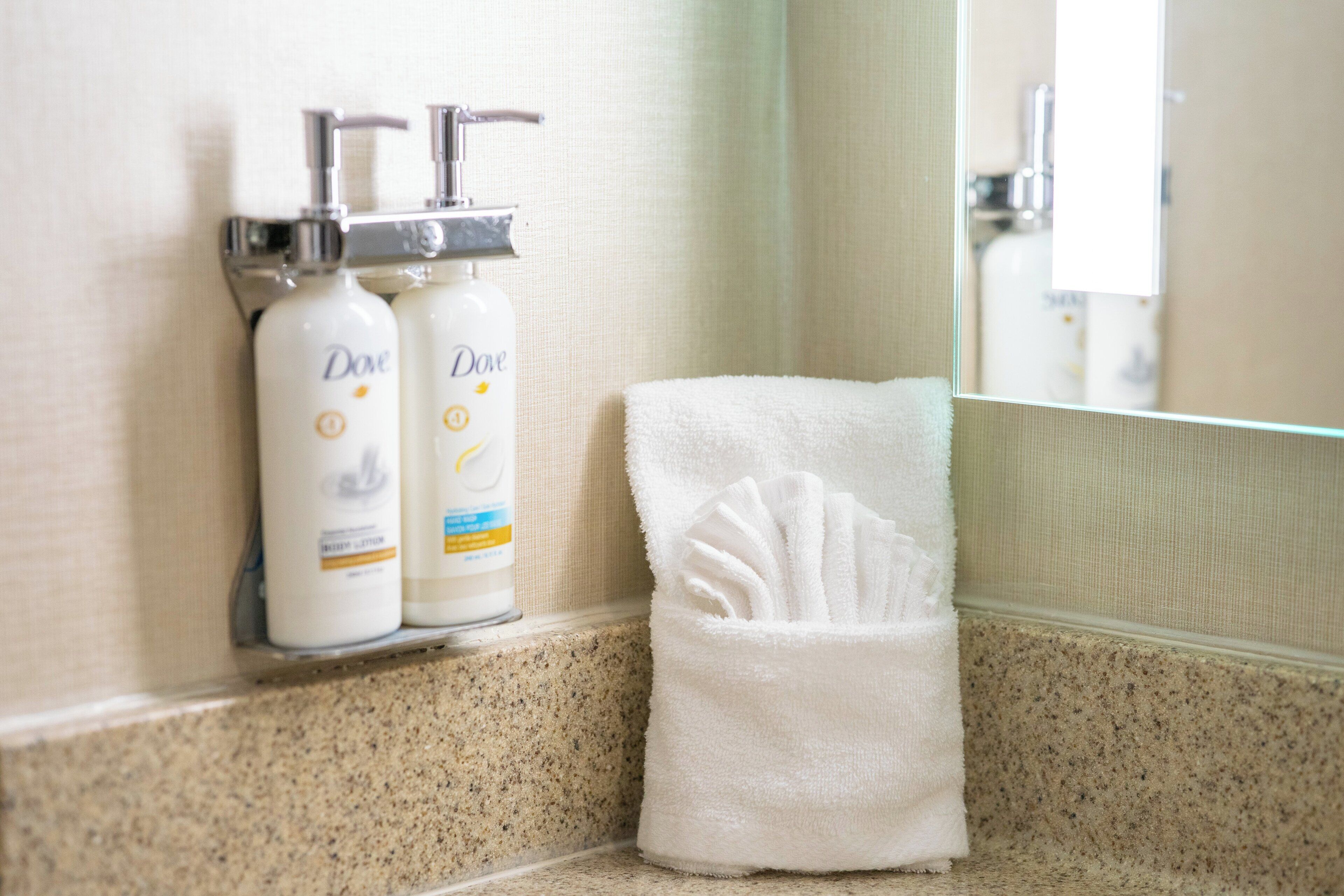 A bathroom with a towel rack holding a white towel and two Dove lotion bottles.