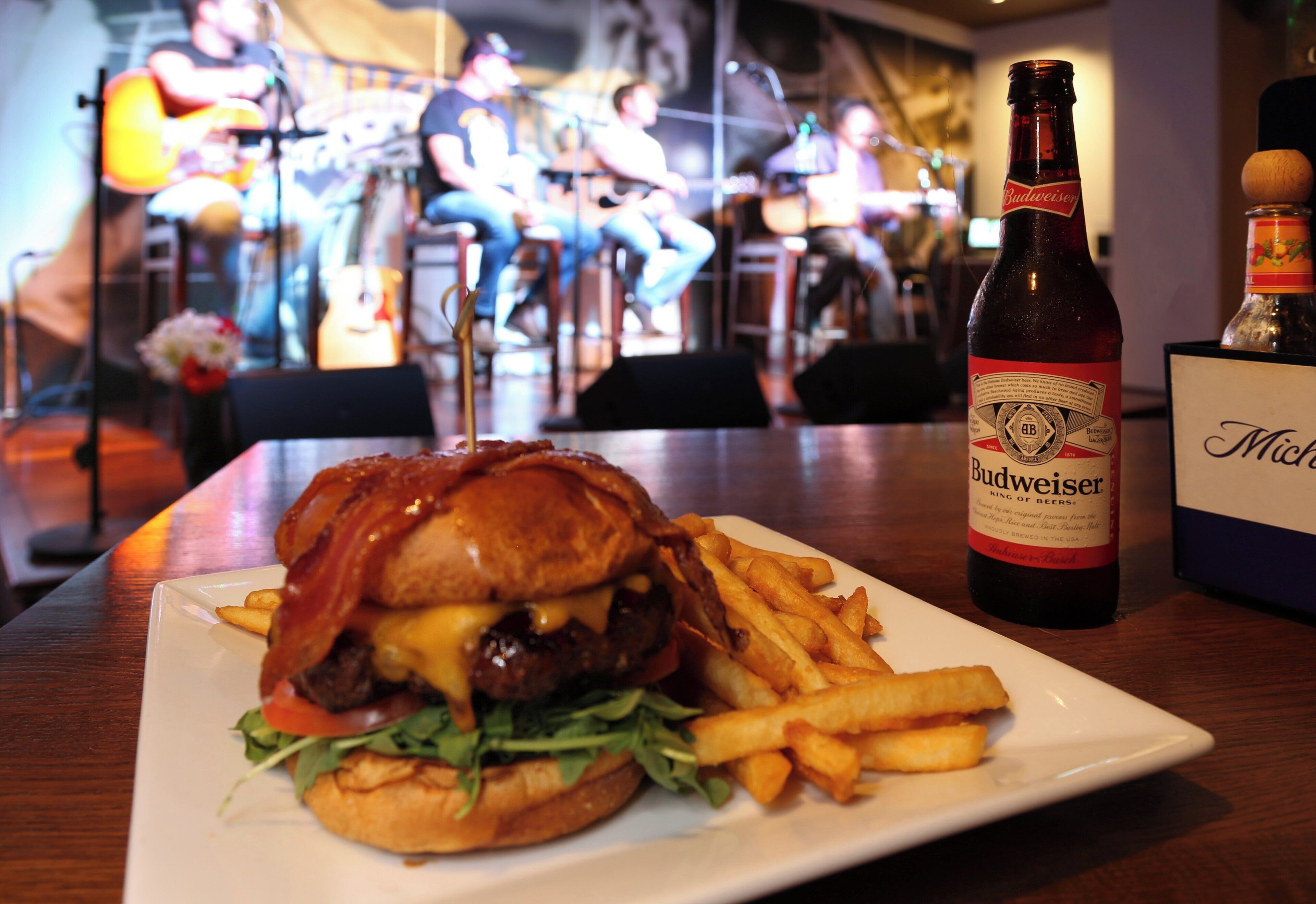Une assiette avec un hamburger et des frites, une bouteille de bière Budweiser et une pancarte portant le nom « Mike ».