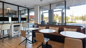 Een modern café met een zithoek, inclusief een bank en ronde tafels, een toonbank met etalage en grote ramen met uitzicht op de straat.