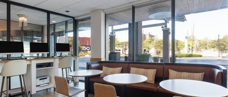 A modern cafe with a seating area featuring a sofa and round tables, a counter with a display, and large windows offering a view of the street.