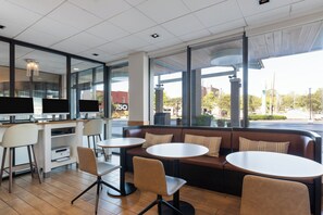 A modern cafe with a seating area featuring a sofa and round tables, a counter with a display, and large windows offering a view of the street. - Holiday Inn Nashville - Vanderbilt (Dwtn) by IHG (Nashville)