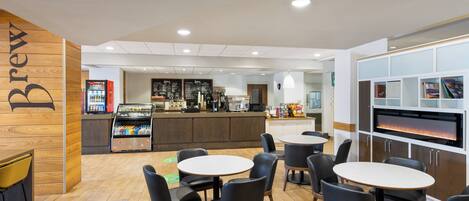 A modern cafe with round tables and chairs, a coffee machine, and a menu board.