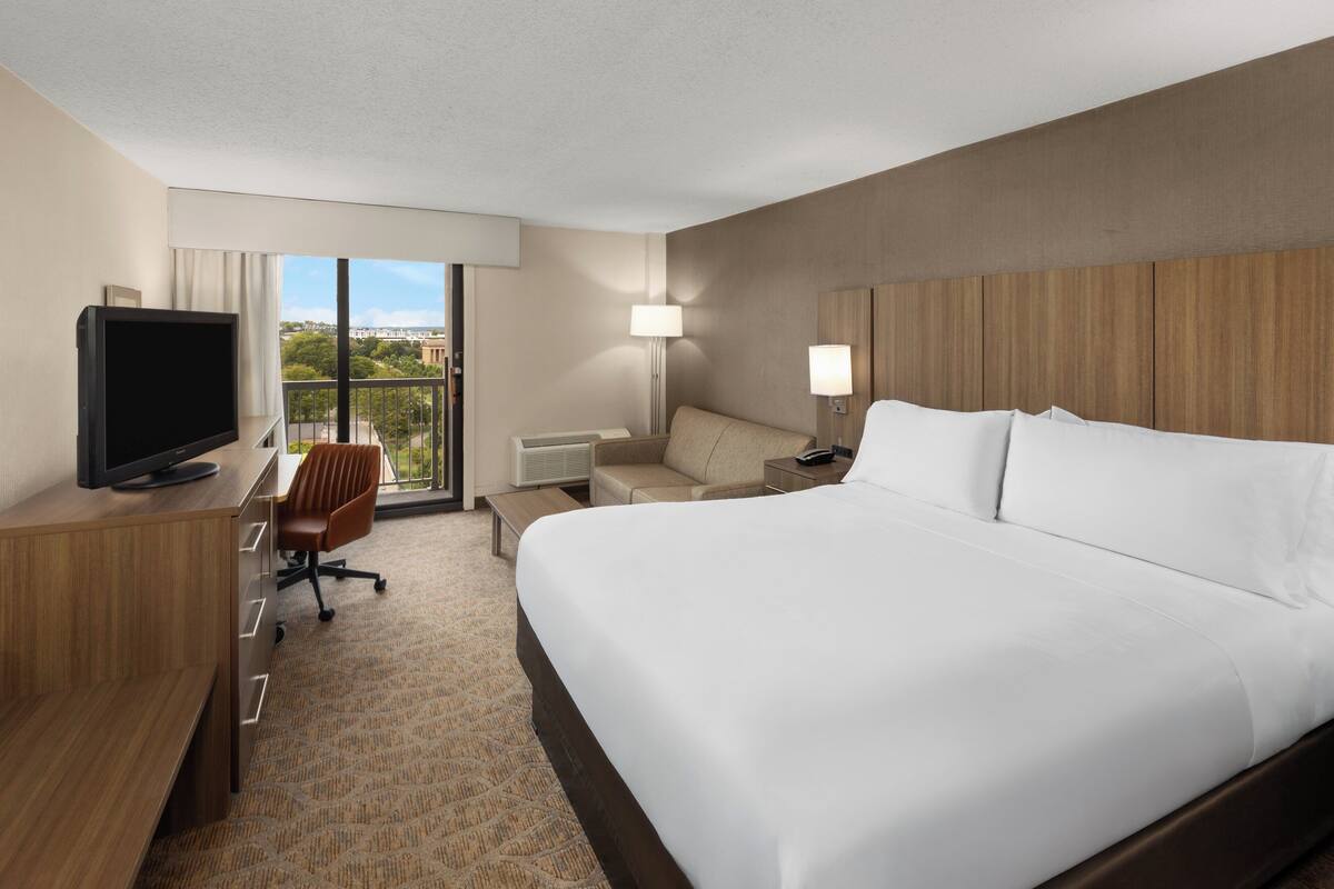 Een hotelkamer met een groot bed, een bureau met een televisie, een stoel, een bank en een lamp.