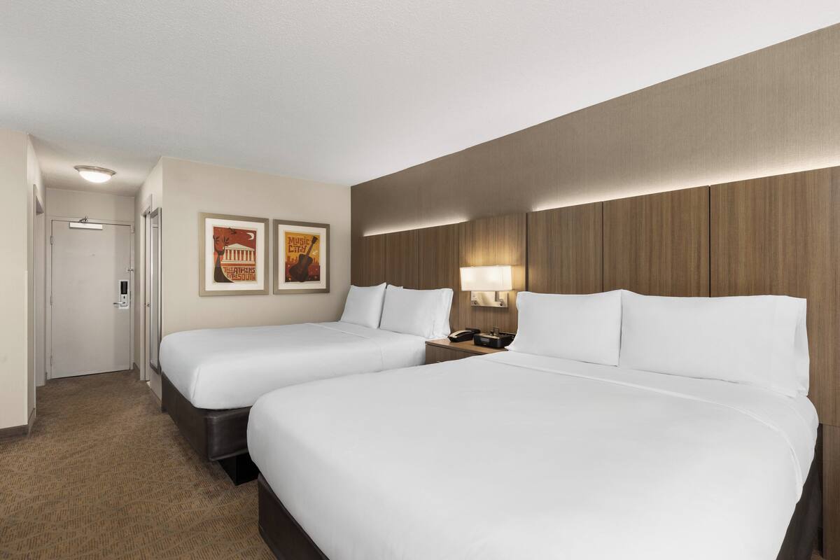 Een hotelkamer met twee eenpersoonsbedden, een deur, een aan de muur bevestigde lamp en twee ingelijste foto's.