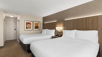 A hotel room with two single beds, a door, a wall-mounted lamp, and two framed pictures.