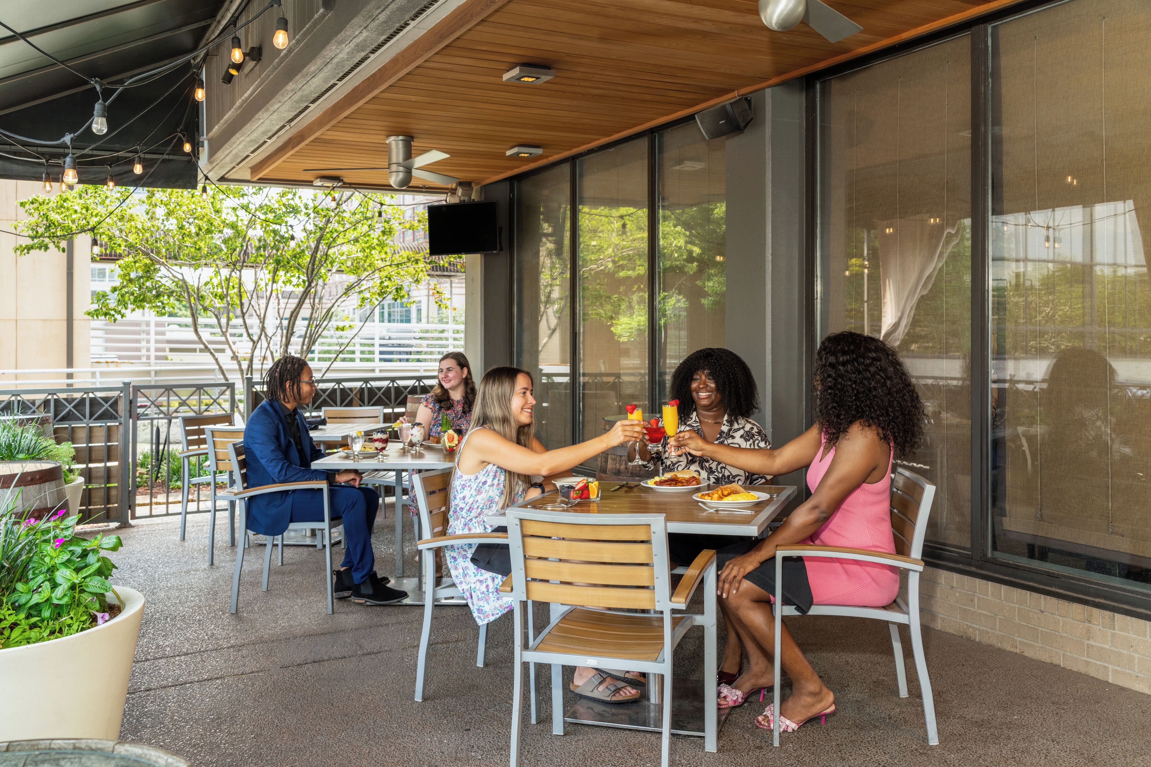 An outdoor café with tables and chairs, large windows, and a view of the city.