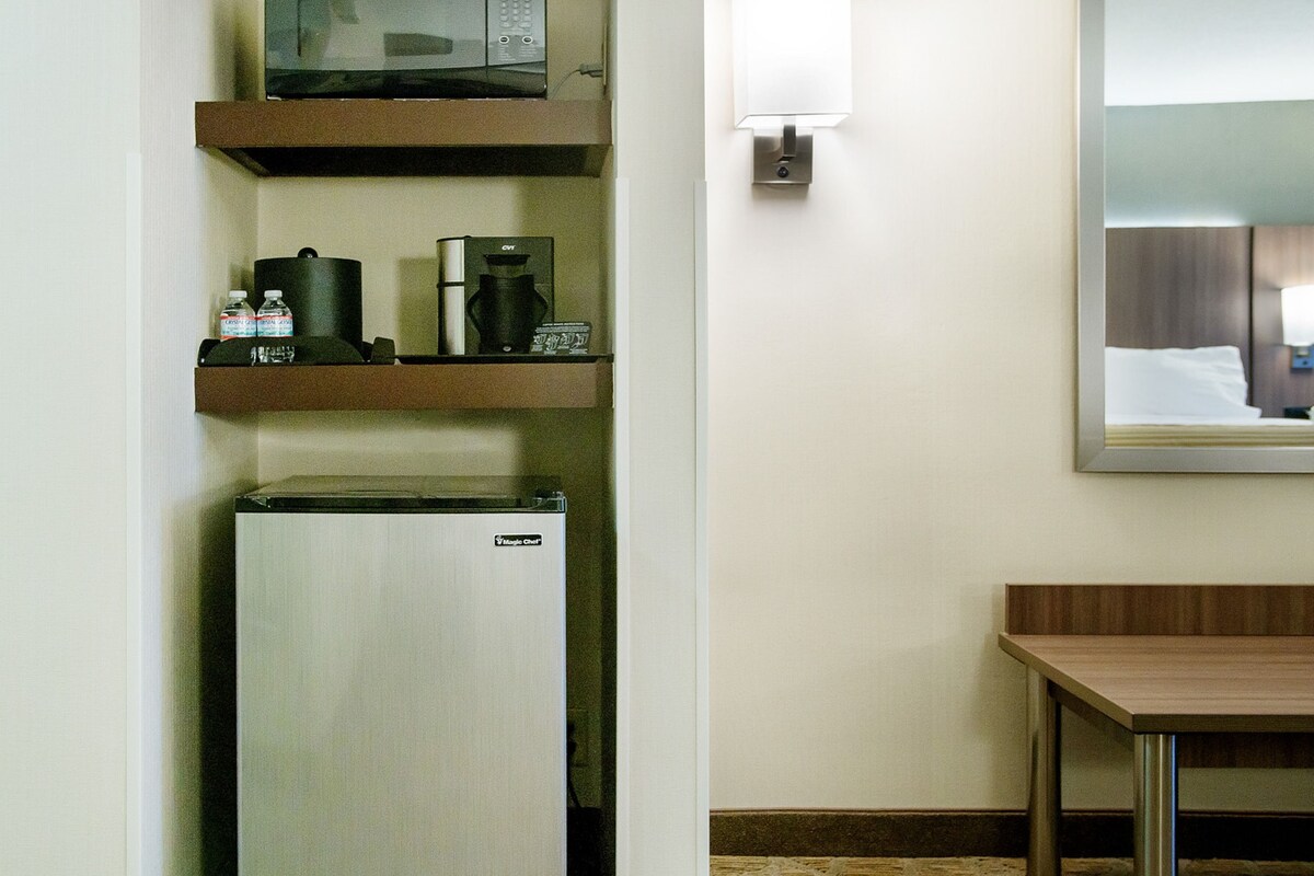 A compact kitchenette with a refrigerator, microwave, and coffee maker on a shelf.