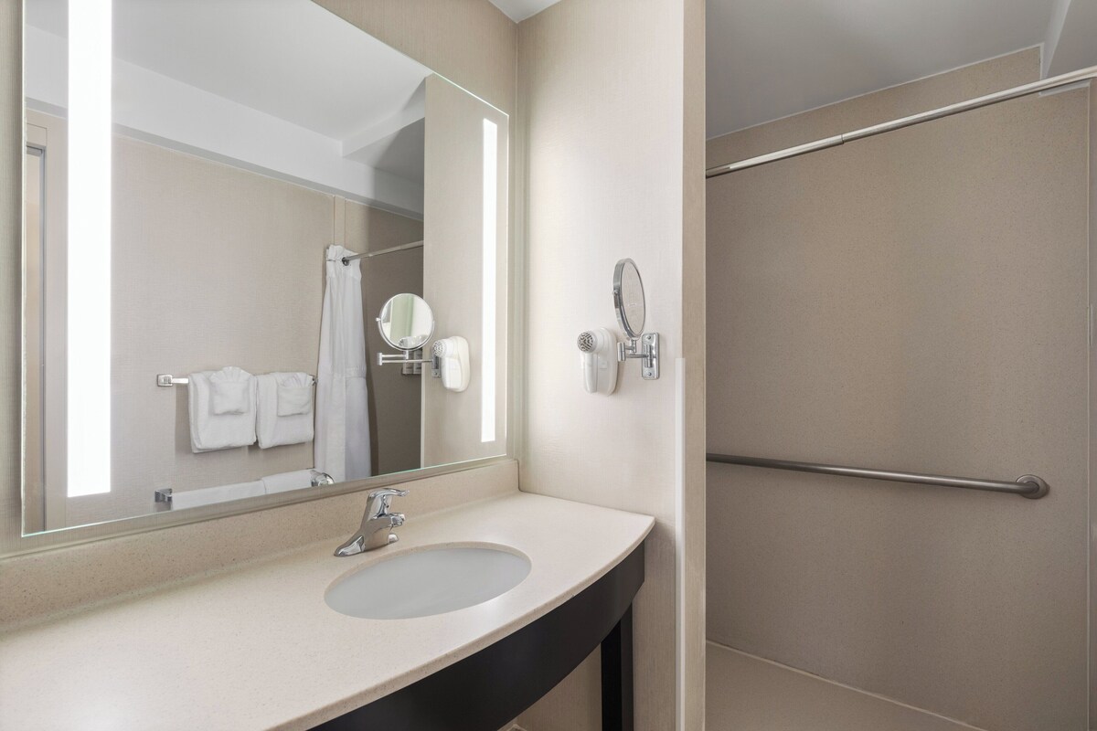 A bathroom with a sink, mirror, towel rack, and a shower area.