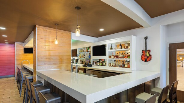 Een moderne barruimte met een lange toonbank, barstoelen en diverse flessen drank.