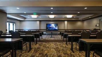 A conference room with a large screen, multiple tables, and chairs arranged for a meeting.
