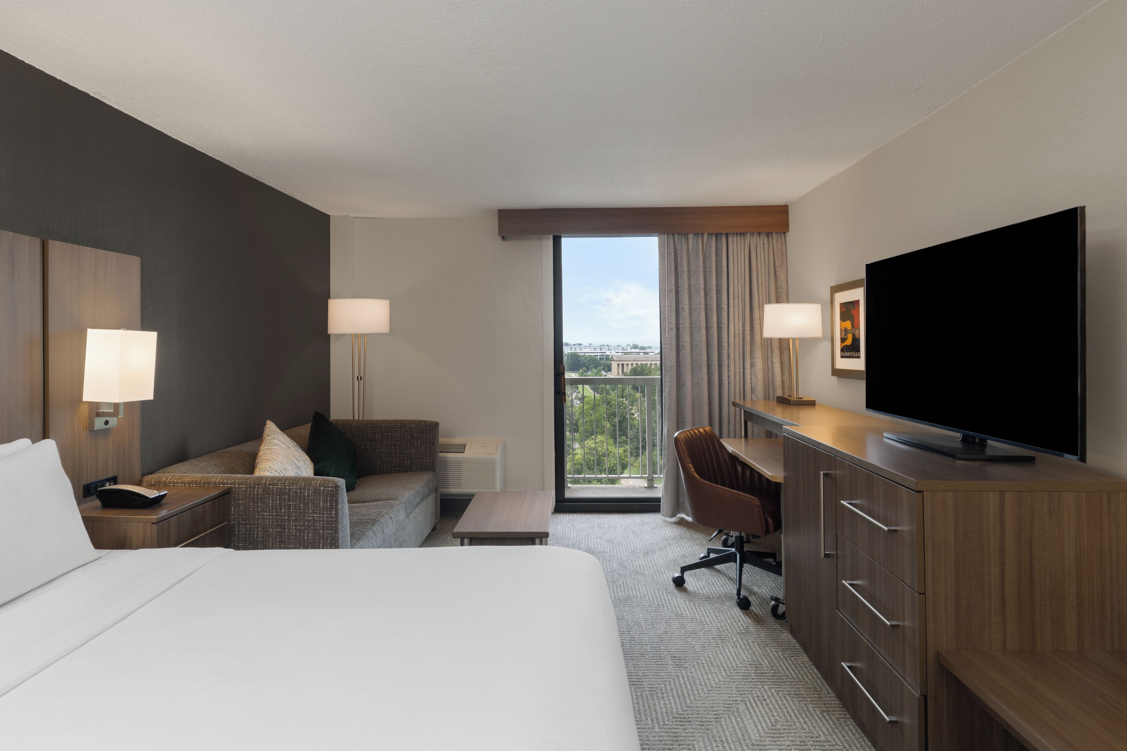 Ein Hotelzimmer mit Bett, einer Couch, einem Schreibtisch, einem Fernseher und Blick ins Freie.