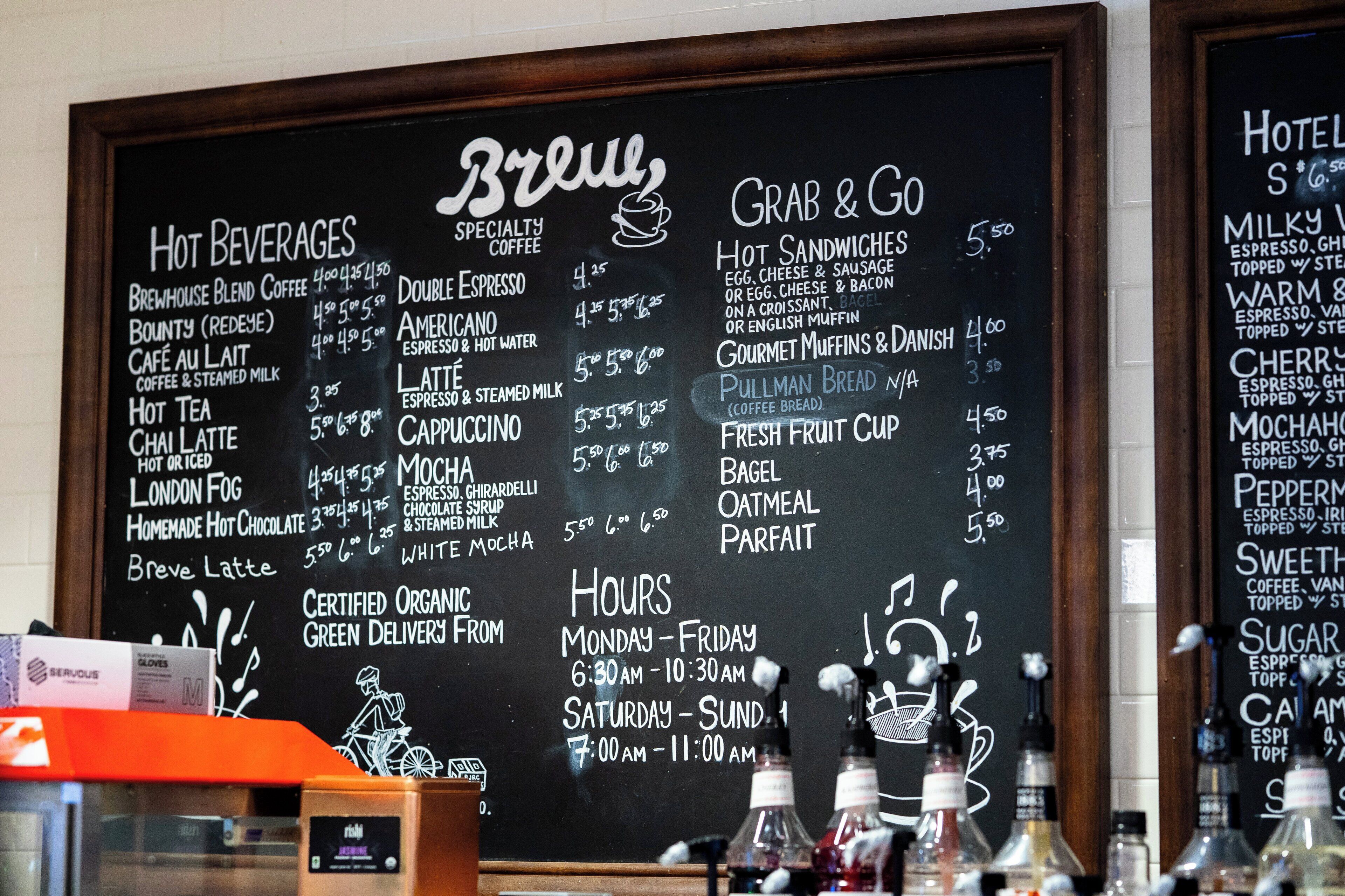 Un pizarrón con el menú que muestra diferentes opciones de café y comida, incluyendo precios y un apartado con los horarios de atención.