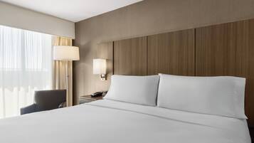 A hotel room with a large bed, a bedside table with a lamp, a chair, and a window with curtains.