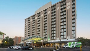 Een hotel met meerdere verdiepingen, met een modern ontwerp, inclusief een overdekte ingang en een parkeerplaats met diverse auto's.