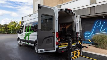 A white van with a green logo parked in front of a building with a neon sign.
