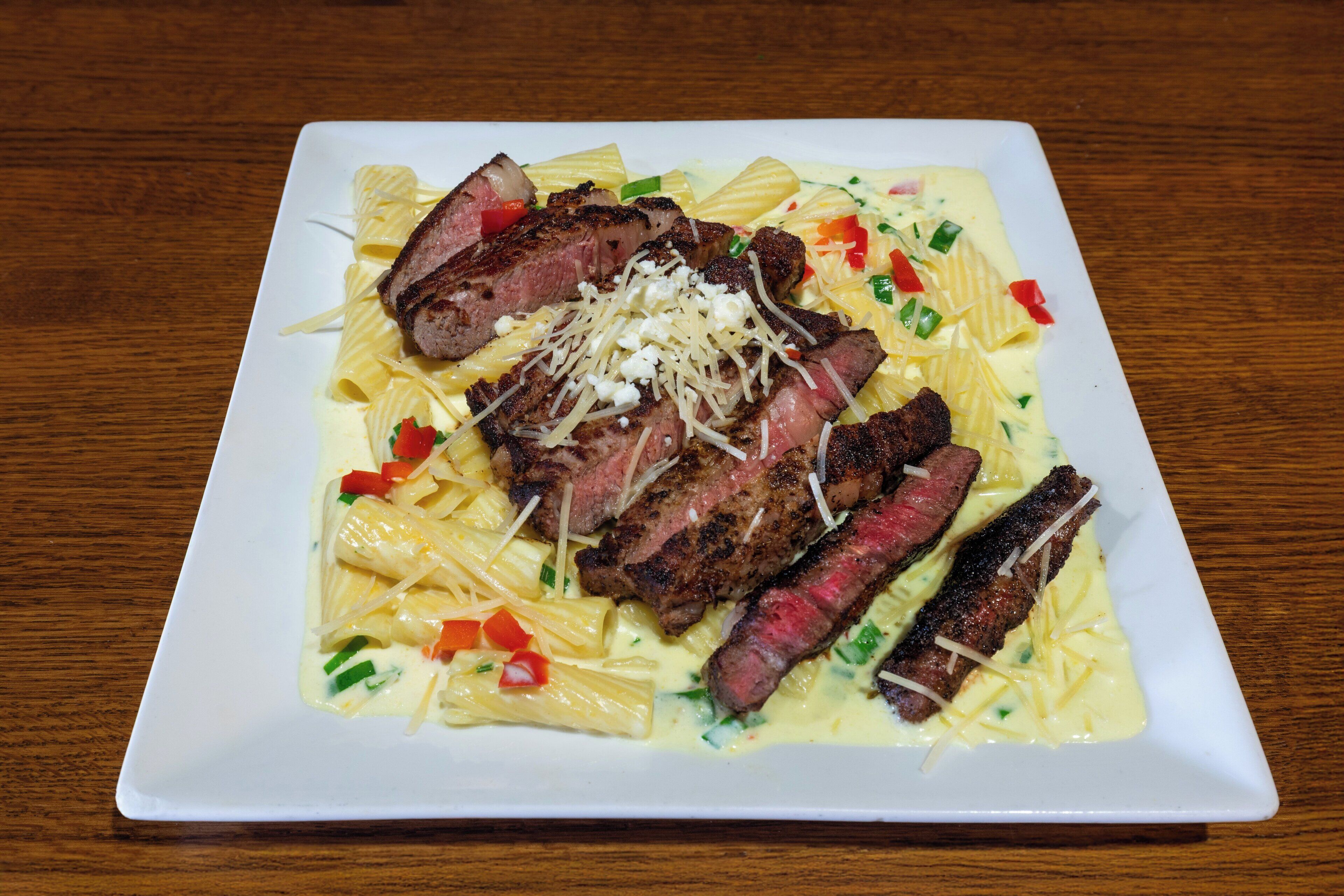 Un plato blanco con pasta, carne y queso sobre una mesa de madera.