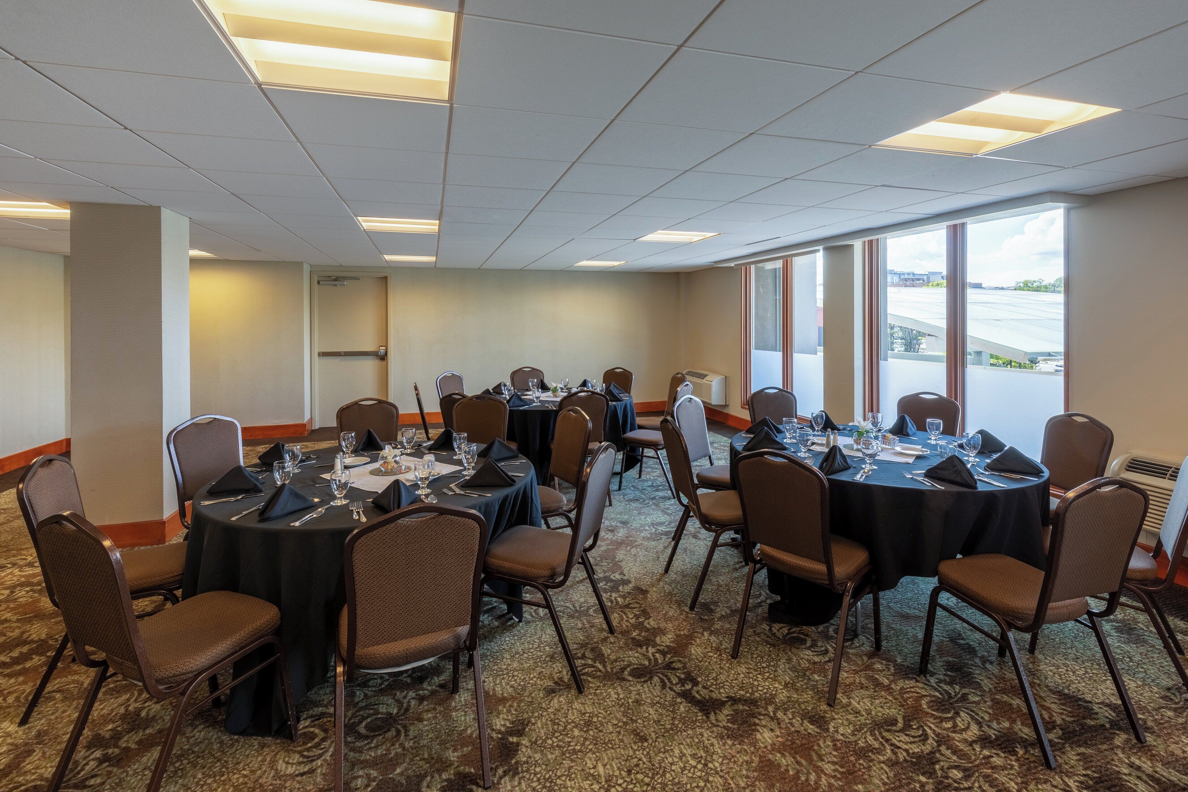 A conference room with round tables, chairs, and a carpeted floor.