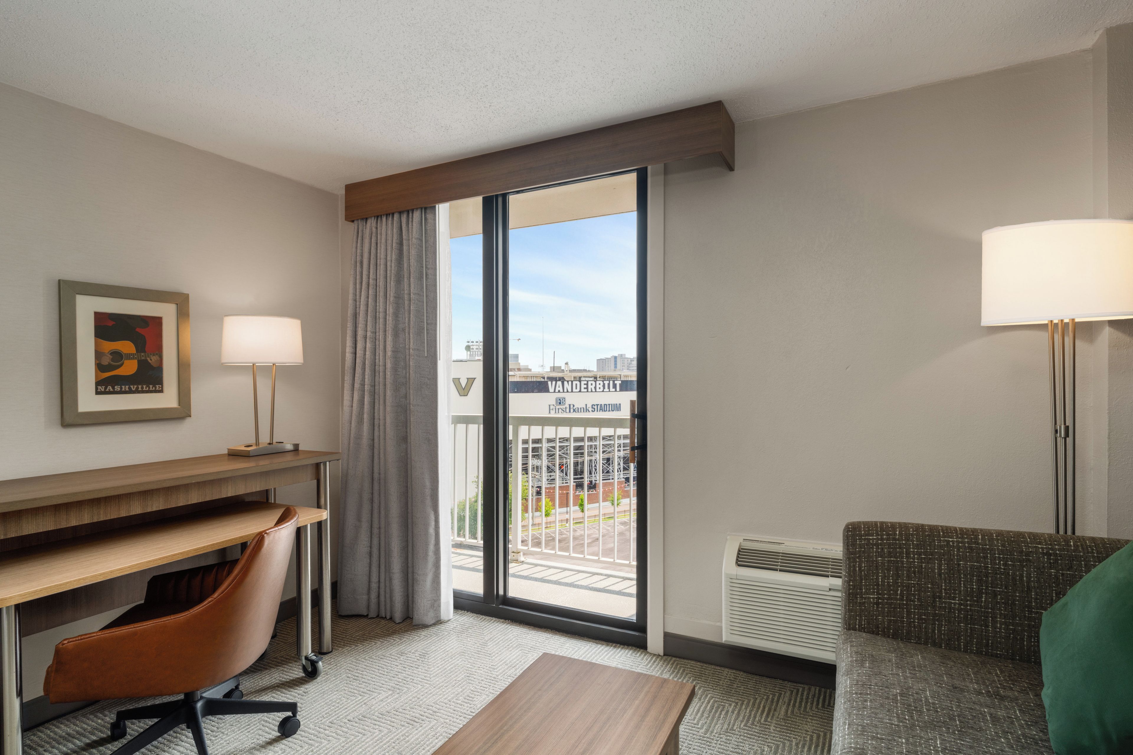 Habitación de hotel con escritorio, silla, sofá y vista al Estadio Vanderbilt.