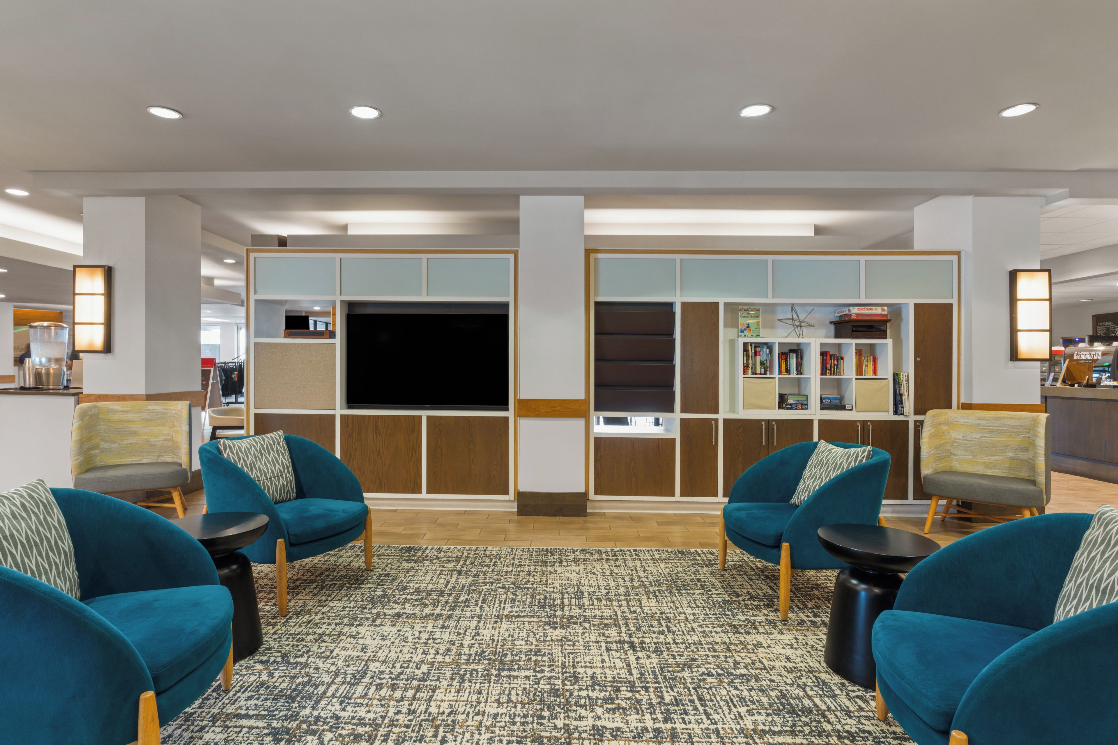 A modern lobby with teal armchairs, a flat-screen TV, and a bookshelf.