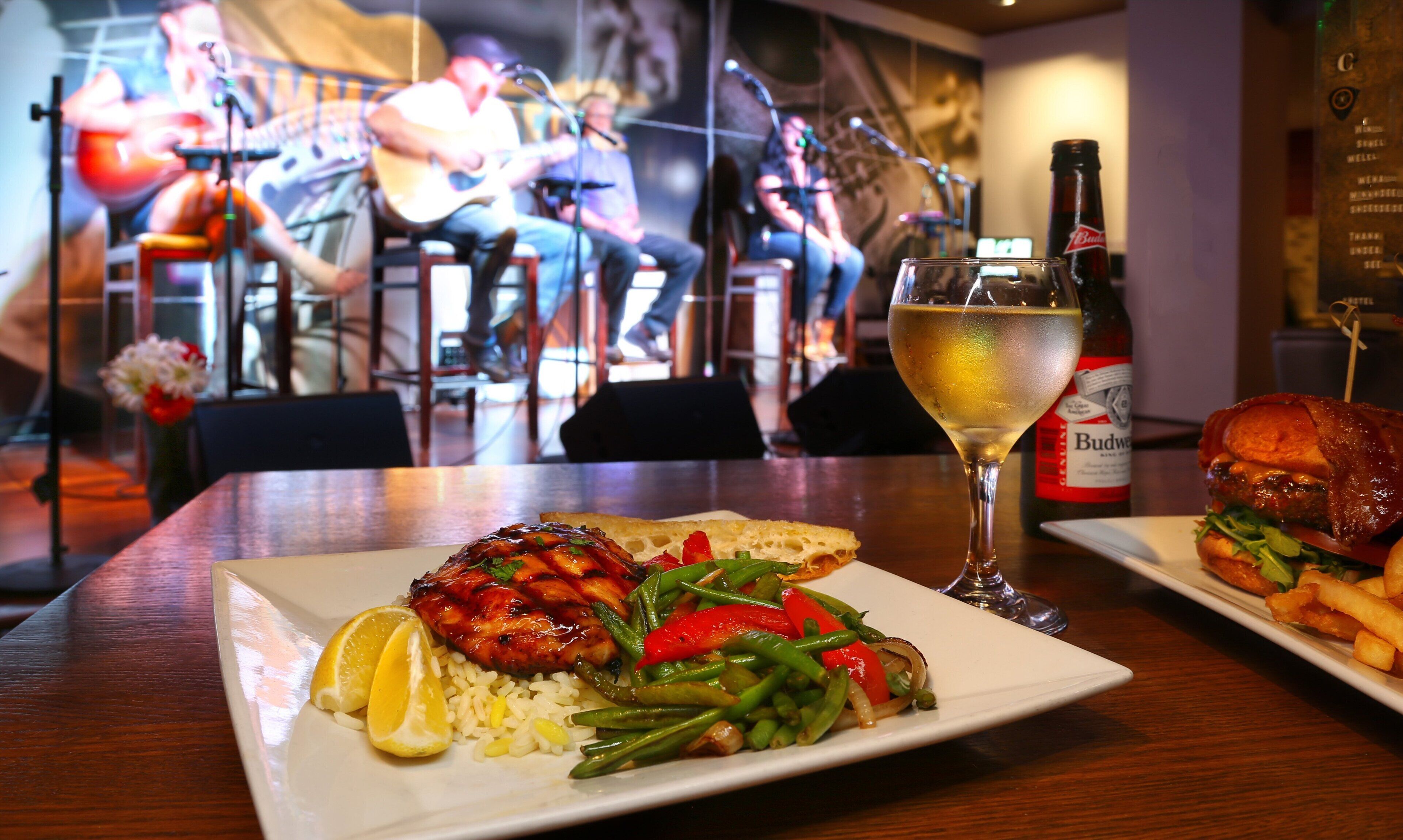 Un ristorante con un piatto di cibo, un bicchiere di vino e una bottiglia di birra Budweiser.