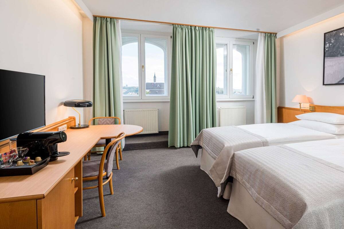 Een hotelkamer met twee bedden, een bureau met koffiezetapparaat, een televisie en een schilderij aan de muur.
