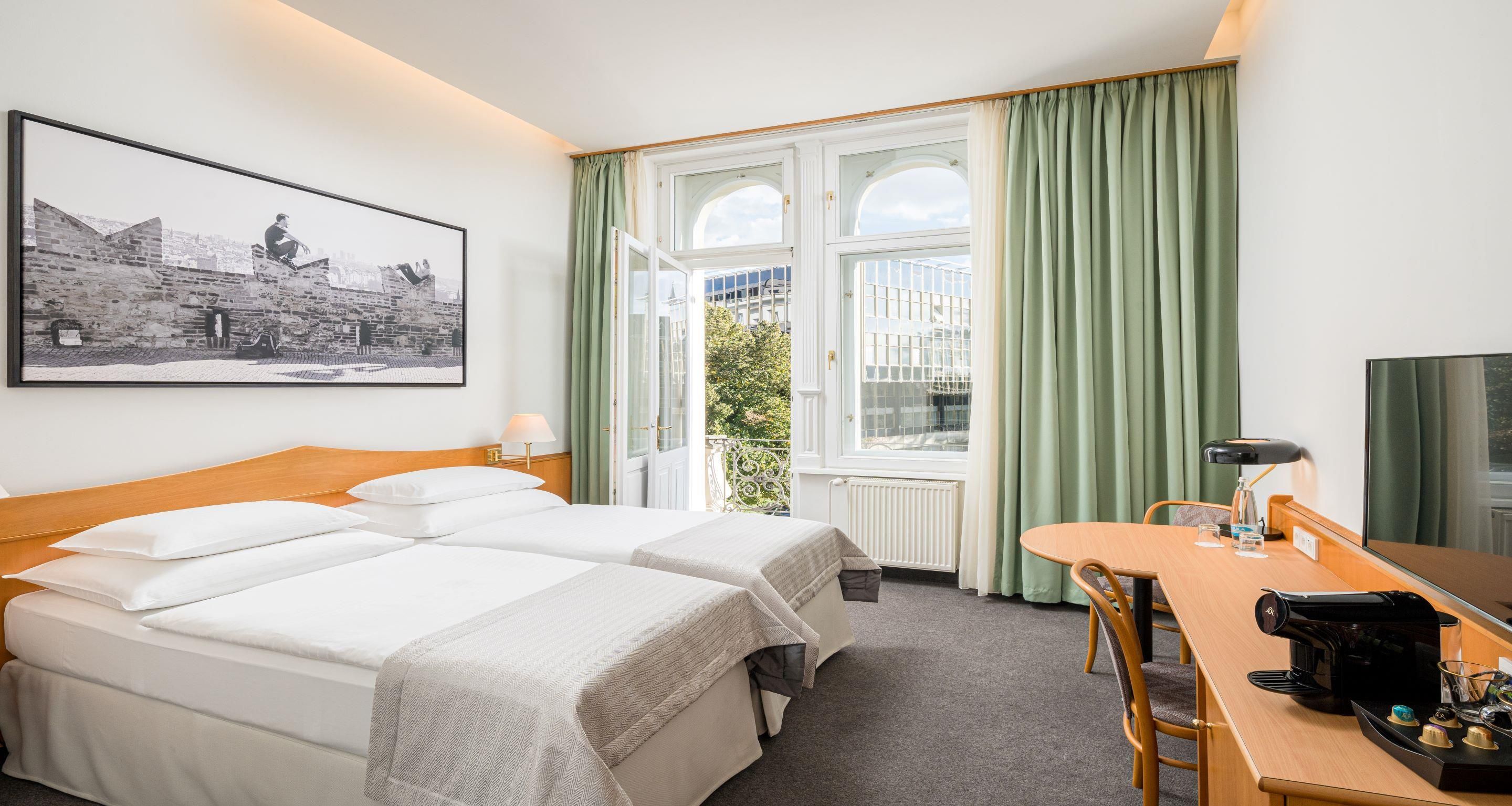 Ein Hotelzimmer mit zwei Betten, einem Esstisch, einer Kaffeemaschine und einem großen Fenster mit Vorhängen.