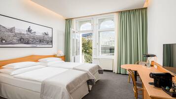 Ein Hotelzimmer mit zwei Betten, einem Esstisch, einer Kaffeemaschine und einem großen Fenster mit Vorhängen.