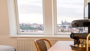 A hotel room with a large window overlooking a cityscape, a table with a coffee maker, and a chair. - Best Western Hotel Moran (Prague)