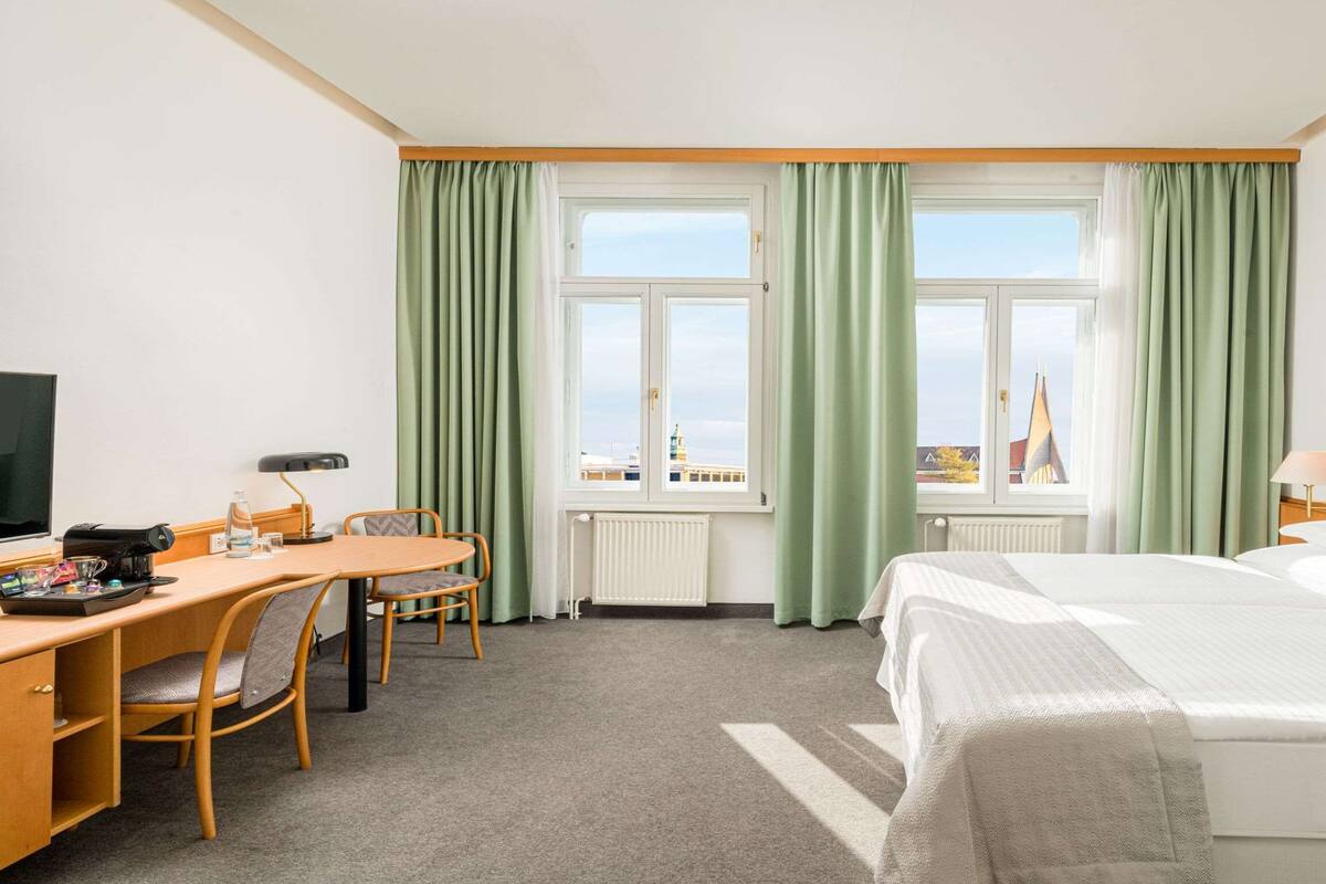 Een hotelkamer met een bed, een bureau met stoel, een televisie en een raam met gordijnen.