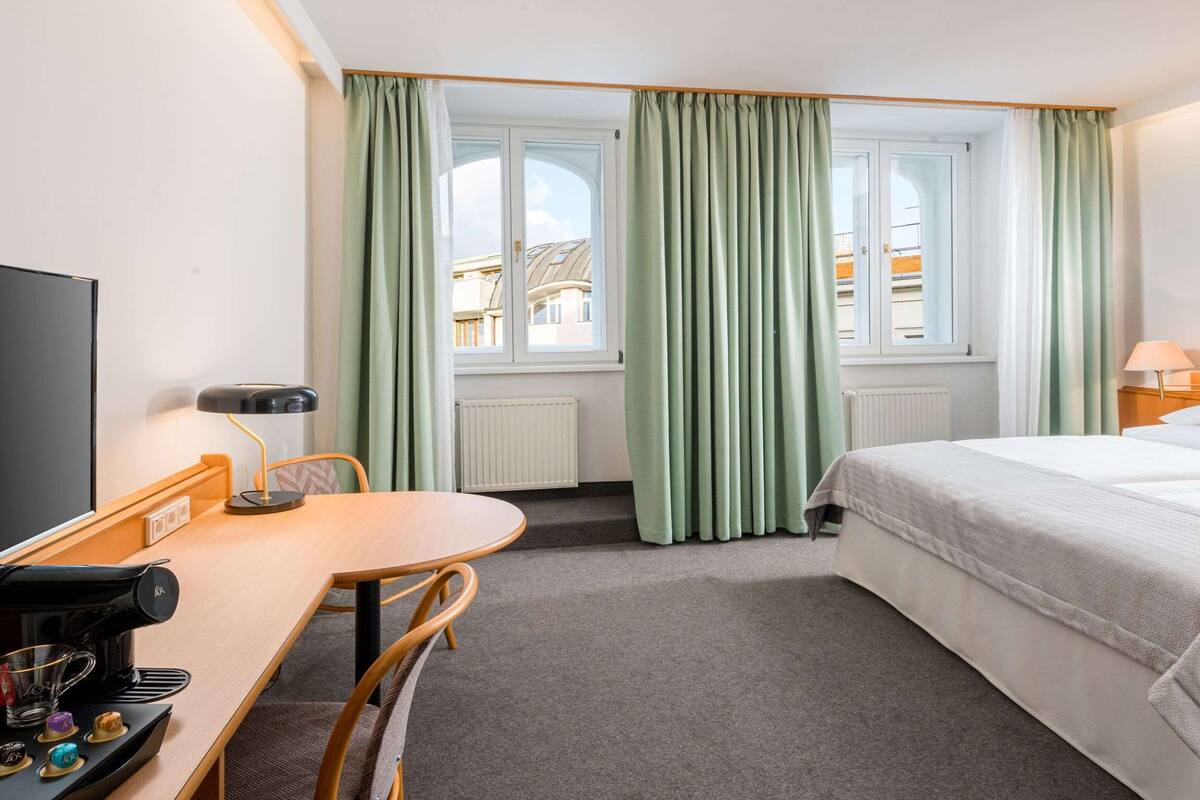 Hotelkamer met een bed, een bureau met koffiezetapparaat, een stoel, een televisie en een raam met gordijnen.