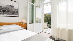 A hotel room with a bed, a nightstand, a lamp, a door leading to a balcony, and a framed picture on the wall. - Best Western Hotel Moran (Prague)