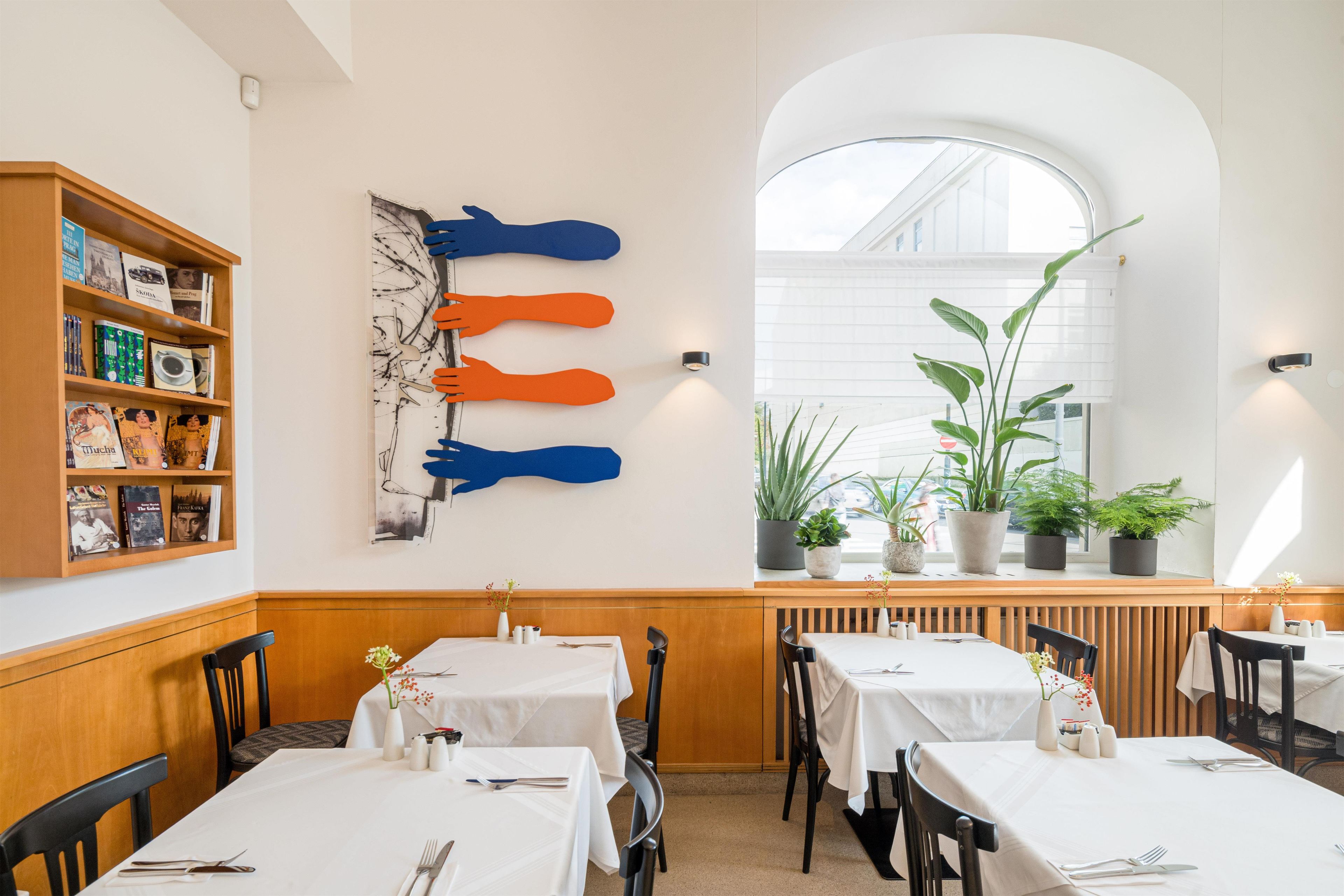 A restaurant interior with tables, chairs, a bookshelf, and a wall art piece.