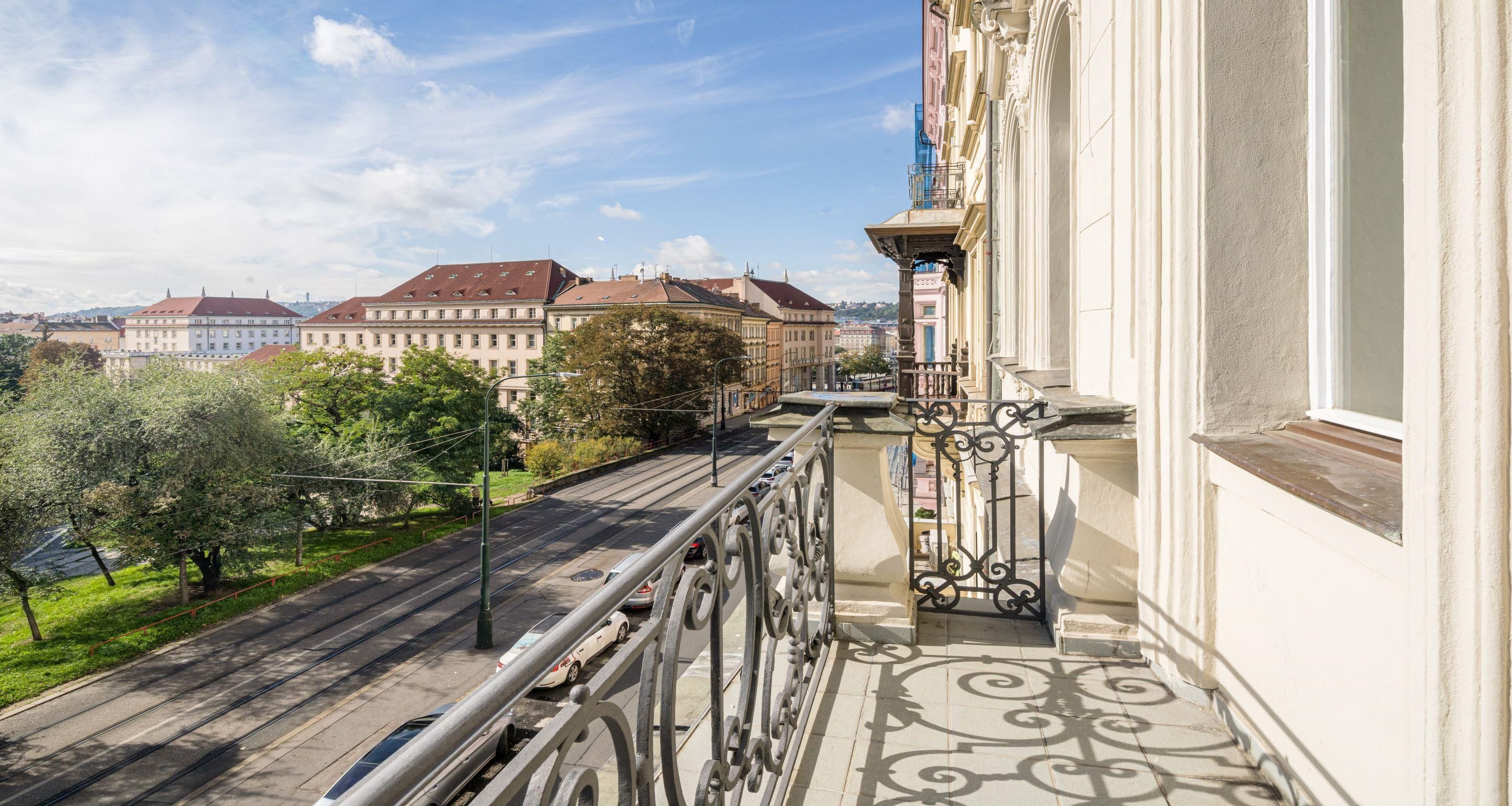 Un balcón con vistas a un paisaje urbano, que incluye edificios y una línea de tranvía.