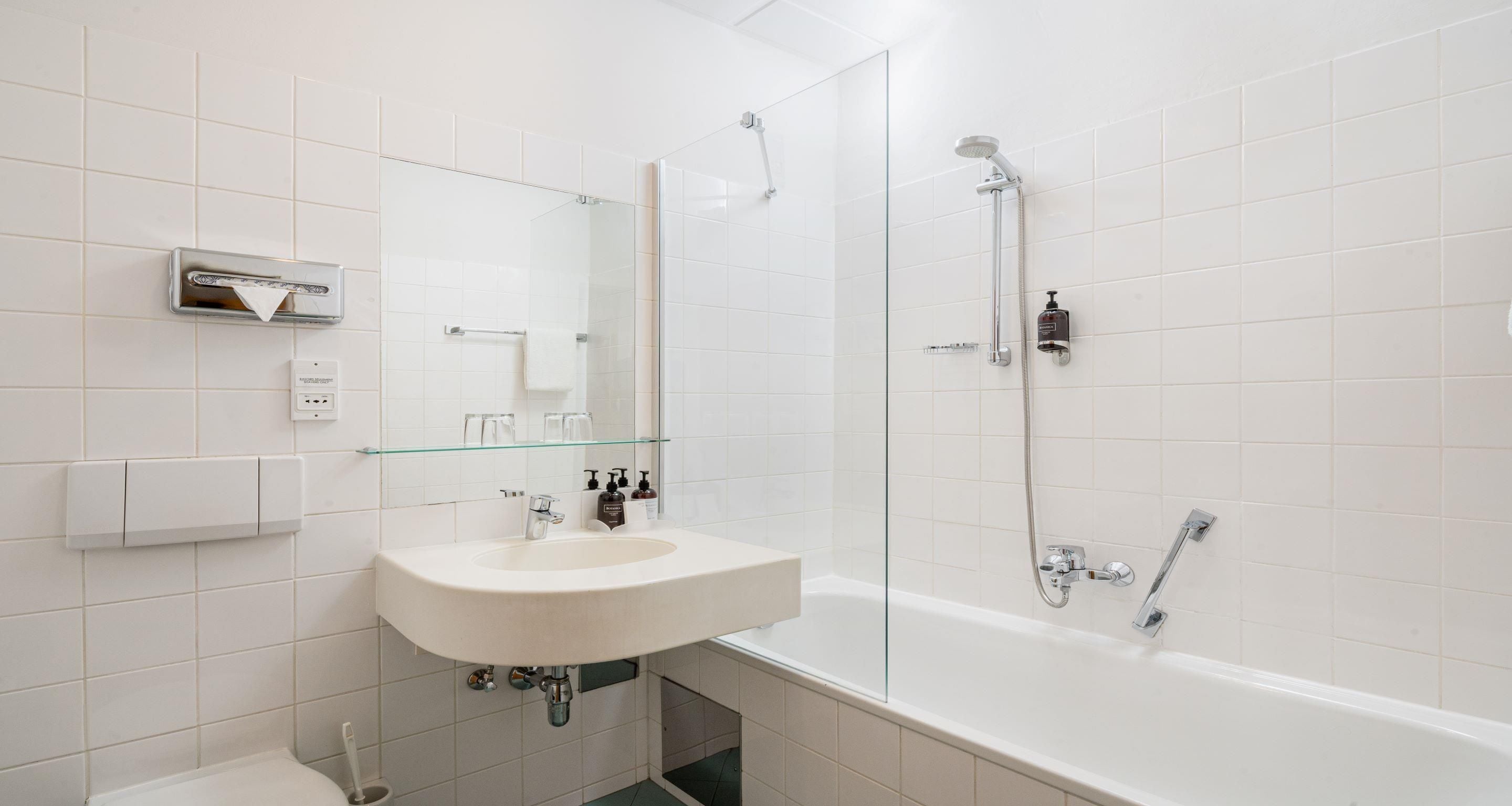 Un baño moderno con lavamanos, espejo y ducha blancos.