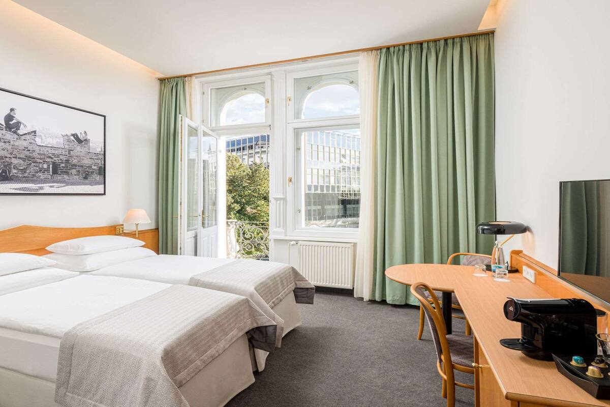 Een hotelkamer met twee bedden, een eettafel, een koffiezetapparaat en een groot raam met gordijnen.